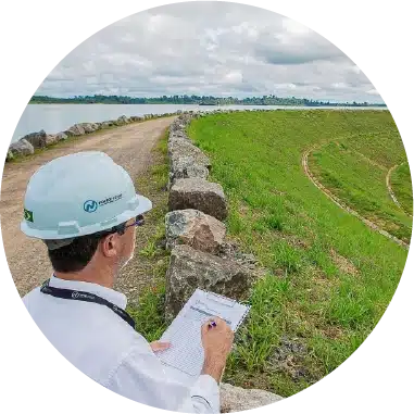 <p>A Usina Hidrelétrica Belo Monte opera conforme a Lei nº 12.334/2010 e a Lei nº 14.066/2020, com um Plano de Segurança de Barragens (PSB) e um Plano de Ação de Emergência (PAE), colaborando com as Defesas Civis locais. O PSB, monitorado pela Aneel, utiliza um sistema avançado que inclui 2.640 instrumentos de monitoramento e tecnologias como barco autônomo, drones e sensores para garantir a segurança das estruturas. Em 2023, todas as estruturas foram classificadas como ‘Normais’ na Inspeção de Segurança Regular.</p>
<p>O projeto da UHE Belo Monte foi reconhecido com o 1º lugar no 5º Simpósio Internacional de Barragens de Enrocamento, destacando-se globalmente pela inovação e boas práticas operacionais. O RoboMAX, introduzido em 2023, modernizou a manutenção dos diques, reduzindo riscos e emissões. Além disso, o Sistema de Notificação de Emergência (SNE) na Zona de Autossalvamento foi aprimorado com 34 sirenes e conectividade para mais de 350 moradores, fortalecendo a segurança e beneficiando as comunidades locais.</p>
